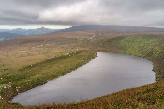 View on lake Lough Bray from top of the hill, Sugarloaf and mountain range in background. Moody, dramatic storm clouds in Wicklow Mountains, Ireland
