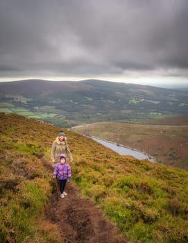 Mother and daughter hiking on a hilltop around the lake, Lough Bray, surrounded by dramatic storm clouds. Family hiking in Wicklow Mountains, Ireland