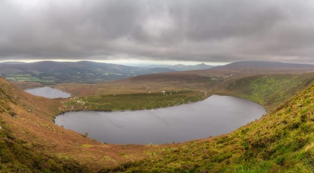 Panoramic view on upper and lower lakes Lough Bray, Sugarloaf and mountain range. Moody, dramatic storm clouds in Wicklow Mountains, Ireland