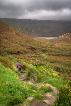 Mother and daughter hiking down the path to lake, Lough Bray, surrounded by storm clouds. Family hiking in Wicklow Mountains, Ireland