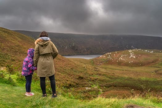 Mother and daughter standing and looking at lake, Lough Bray surrounded by dramatic storm clouds and sky. Family hiking in Wicklow Mountains, Ireland