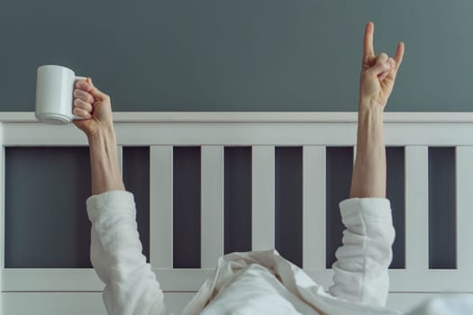 Wonderful start to new day. Unrecognizable man wakes up and stretches in comfortable bed, holding cup of fragrant coffee in his hands. Positive emotions. Have great night's sleep.