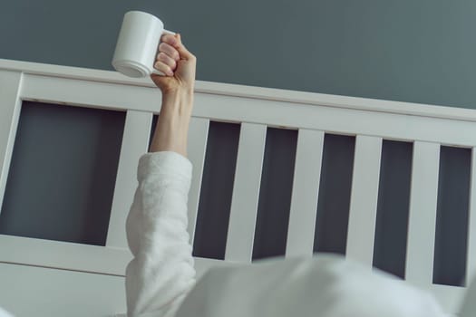 Great mood, first day of vacation. Unrecognizable man wakes up and stretches in comfortable bed, holding cup of fragrant coffee in his hands. Positive emotions. Beginning of day.