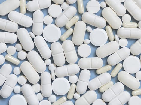 Mix of white medical capsules and pills on light blue top view. Medicinal treatment. Taking dietary supplements and vitamins. Assorted pharmaceutical products