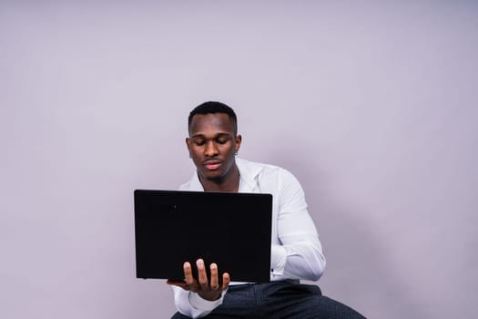 Optimistic african-american male student in a casual shirt using laptop pc isolated