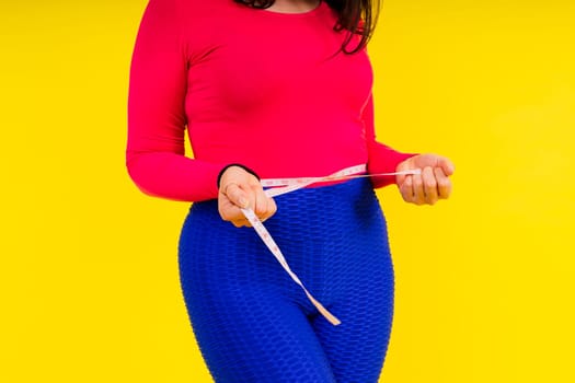 Overweight woman measuring waist before weight loss in a studio shot on yellow background