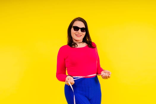 Overweight woman measuring waist before weight loss in a studio shot on yellow background