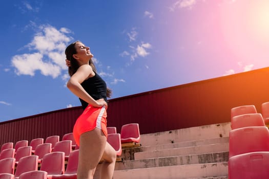 A female coach with dark hair stands on the red running track of the stadium, dressed in sports uniform.