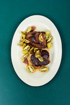 Roasted ostrich steak and mini kiwi on a plate
