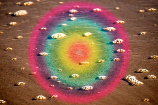 Foam bubbles of the surf on sand with circle of LGBTQ colors
