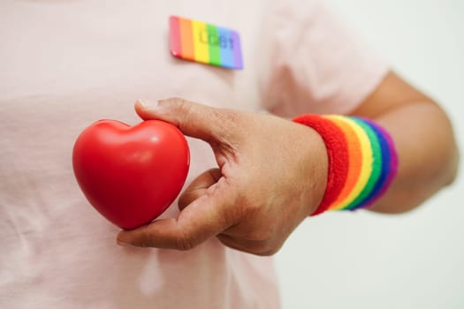 Asian woman holding red heart with rainbow flag, LGBT symbol rights and gender equality, LGBT Pride Month in June.