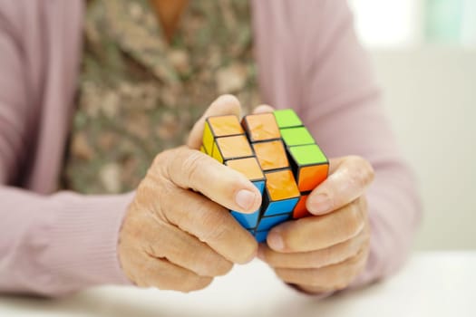 Bangkok, Thailand - May 15, 2022 Asian elderly woman playing Rubik cube game to practice brain training for help dementia prevention and Alzheimer disease.
