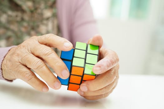 Bangkok, Thailand - May 15, 2022 Asian elderly woman playing Rubik cube game to practice brain training for help dementia prevention and Alzheimer disease.