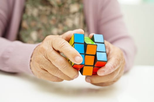Bangkok, Thailand - May 15, 2022 Asian elderly woman playing Rubik cube game to practice brain training for help dementia prevention and Alzheimer disease.