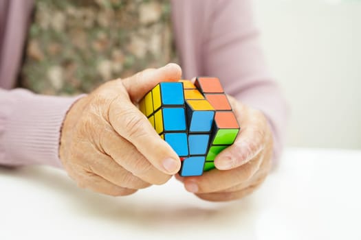 Bangkok, Thailand - May 15, 2022 Asian elderly woman playing Rubik cube game to practice brain training for help dementia prevention and Alzheimer disease.
