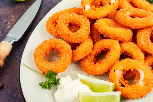 Baked breaded calamari or octopus rings on brown concrete table.