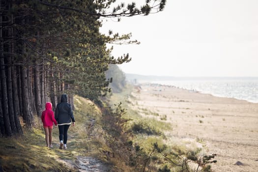 Family walking in forest along beach. Summer vacation trip close to nature. People actively spending leisure time. Back view of woman with daughter enjoying long walk during summertime. Travel concept