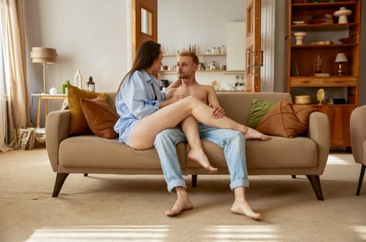 Beautiful sensual woman and sexy man talking together sitting on sofa. Sexy passionate girlfriend and boyfriend at home