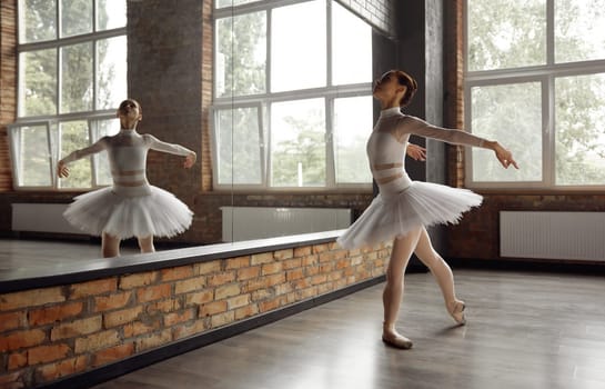 Beautiful young ballerina training classic ballet in studio with huge mirror. Practice routine concept