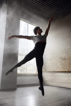 Young stylish modern male ballet dancer in motion. Professional choreographer performing over smoky studio background