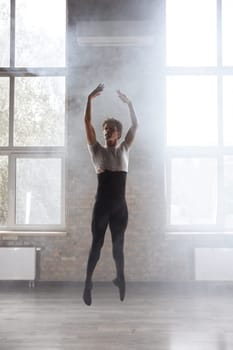 Male ballet dancer performing modern choreography in dance studio. Graceful classical artist in jump over hazy background