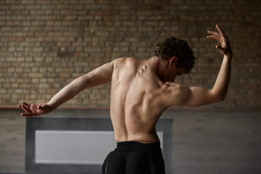 Graceful athletic ballet male dancer demonstrating strong perfect upper body. Shirtless muscular man dance performer view from back