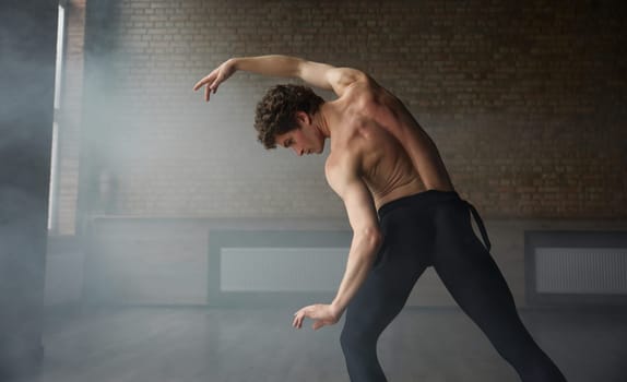 Graceful athletic ballet male dancer demonstrating strong perfect upper body. Shirtless muscular man dance performer view from back
