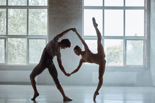 Silhouette of man and woman ballet dancers performing together against studio background. Contemporary choreography performance