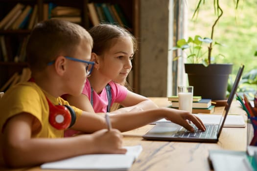 Little schoolchildren studying together using laptop computer. Smart siblings enjoying remote education and e-learning at virtual elementary school. Homeschooling process