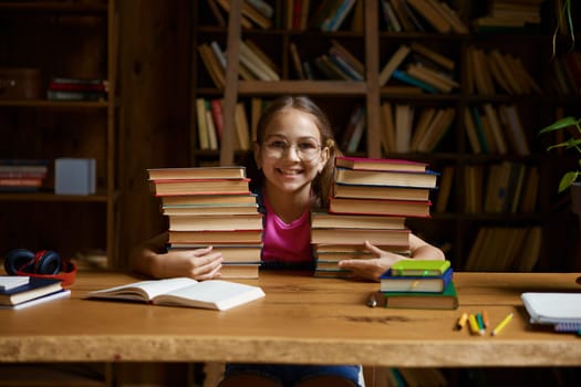 Back to school concept. Happy little schoolgirl leaning on stack on textbooks ready to study hard on remote lessons of virtual classroom platform