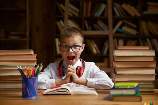 Excited child sitting at desk table with lots of textbook in stack. Online learning problem and difficulties with homework