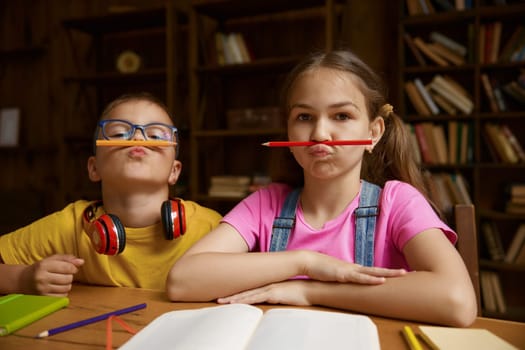 Portrait of cute children holding pencil on mouth under nose. Mischief humor boy and girl siblings feeling playful and fooling around. Happy childhood and interesting home education