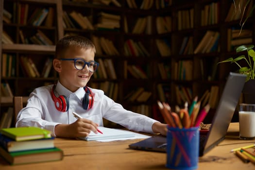 Overwhelmed little schoolboy in headset looking at laptop screen feeling misunderstanding and incomprehension. Difficulties and troubles at virtual lesson concept