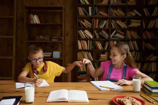 Friendly communication between brother and sister siblings during homeschooling e-learning process. Small girl and boy celebrating success of exam passing remote exam