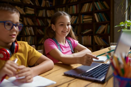 Little schoolchildren studying together using laptop computer. Smart siblings enjoying remote education and e-learning at virtual elementary school