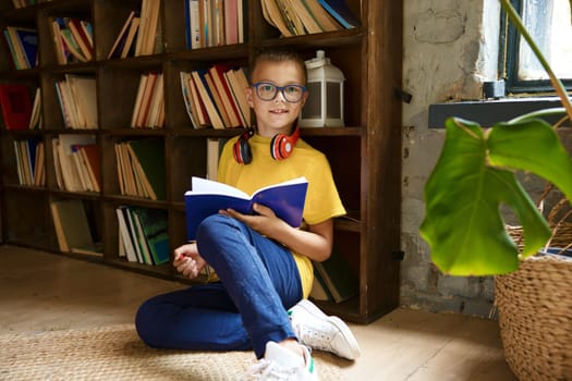 Portrait of happy schoolboy child wearing headset doing creative homework during break time in education process at library. Elementary school student learning language at home