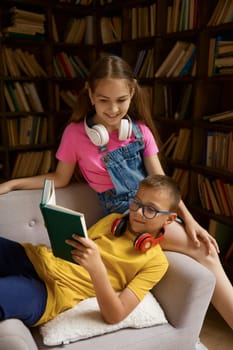Happy brother and sister reading together at home library preparing for exam or doing homework of literature lesson together. Homeschooling process