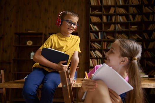 Brother and sister schoolchildren studying at home together. Little boy trying to see what her sibling writing in diary. Family relationships between children concept
