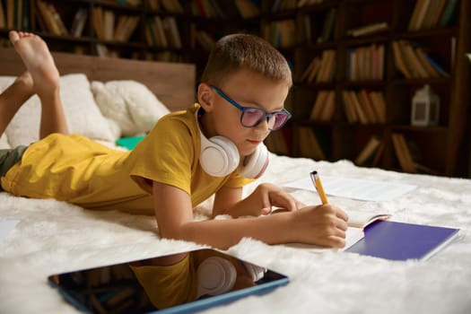 Little boy child using modern digital gadget studying at home while lying in bed. Comfortable education and happy childhood