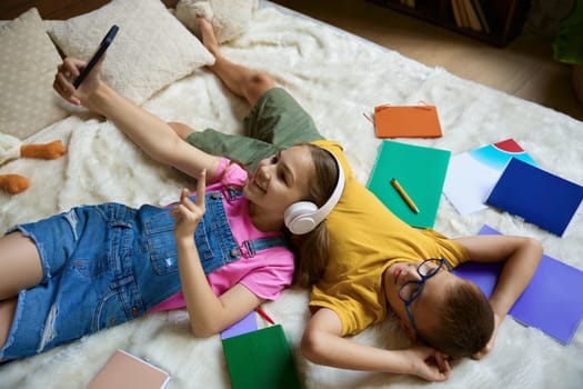 Charming little elementary school student making selfie with mobile camera. Cute girl and boy siblings having rest lying in bed. Nice brother and sister relationships and happy childhood