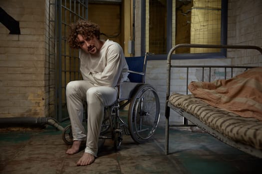 Mentally ill patient wearing straitjacket sitting in wheelchair over psychiatric hospital ward. Crazy man suffering from schizophrenia