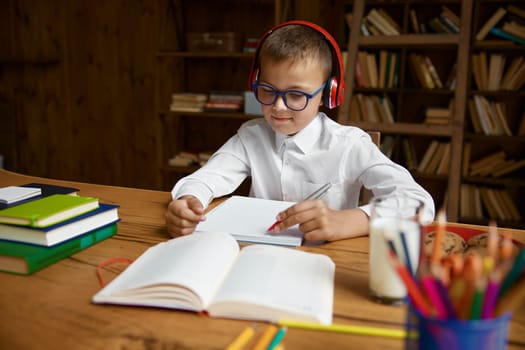 Cute little schoolboy student in headset doing homework with language task. Webcam view on smart pupil studying at virtual lesson using modern technology and wireless internet