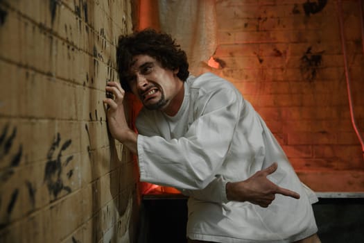 Crazy prisoner or psychiatric hospital patient wearing straitjacket scratching wall with nails. Sick male schizophrenic suffering from strong mental disorder, screaming and crying