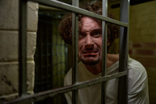 Portrait of caged crazy man with mad face crying bitterly and suffering from mental disorder