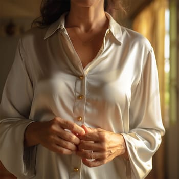 close-up of an unknown woman's hand buttoning a silk blouse. sophistication and elegance, warm lamp illumination