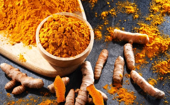 Composition with a bowl of ground turmeric and its fresh rhizome.