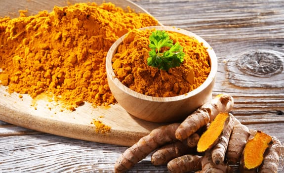 Composition with a bowl of ground turmeric and its fresh rhizome.