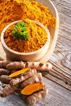 Composition with a bowl of ground turmeric and its fresh rhizome.