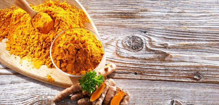 Composition with a bowl of ground turmeric and its fresh rhizome.