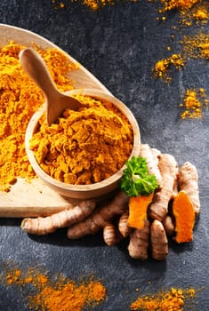 Composition with a bowl of ground turmeric and its fresh rhizome.